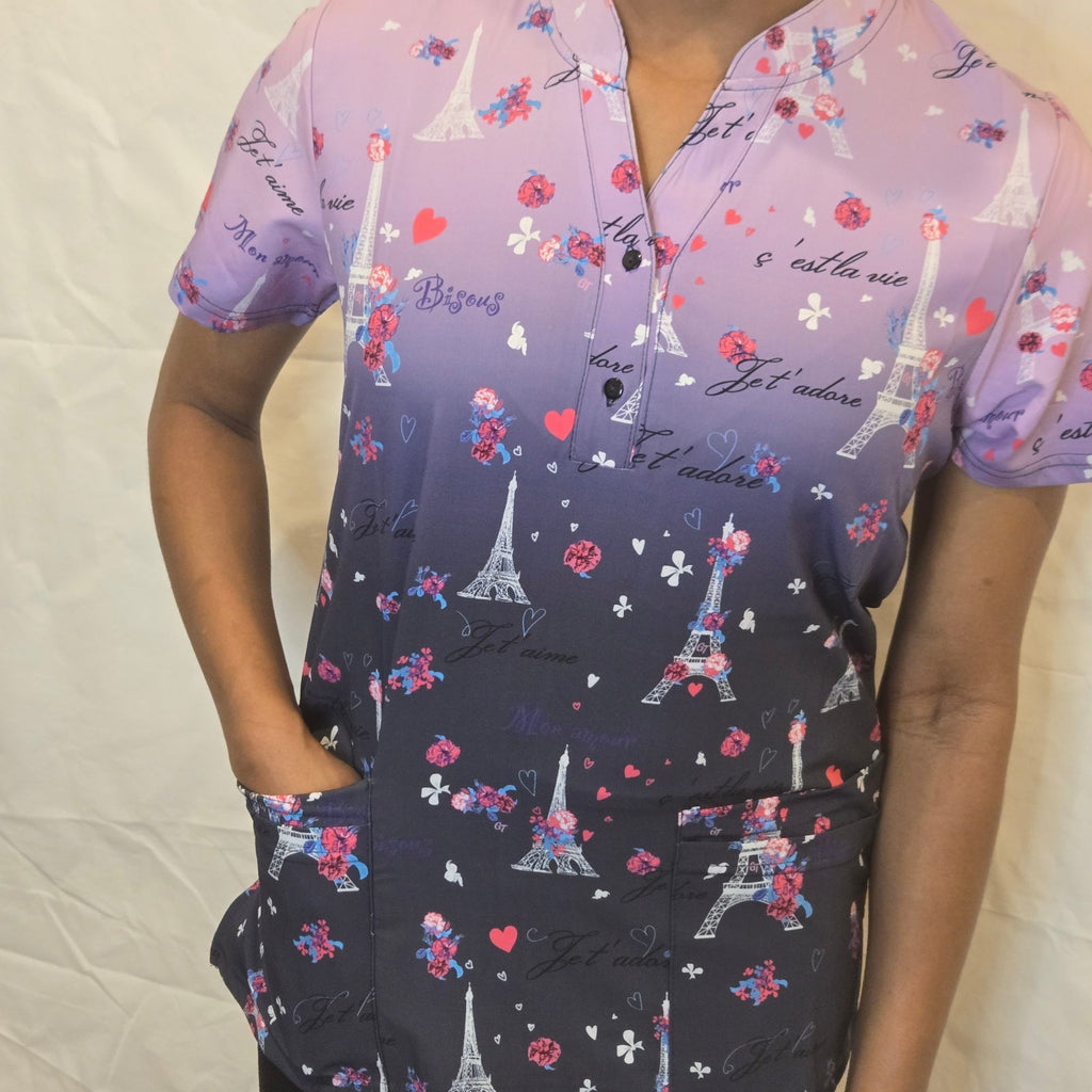 A short-sleeve button-up top with a purple-to-dark-gray gradient and an all-over Paris-themed print featuring Eiffel Towers, roses, hearts, and script text, shown on a model against a wrinkled off-white fabric background.